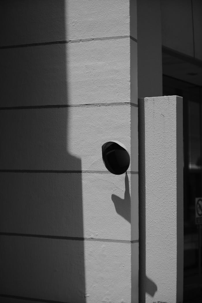 Black and white image of a security camera mounted on a modern urban building wall.